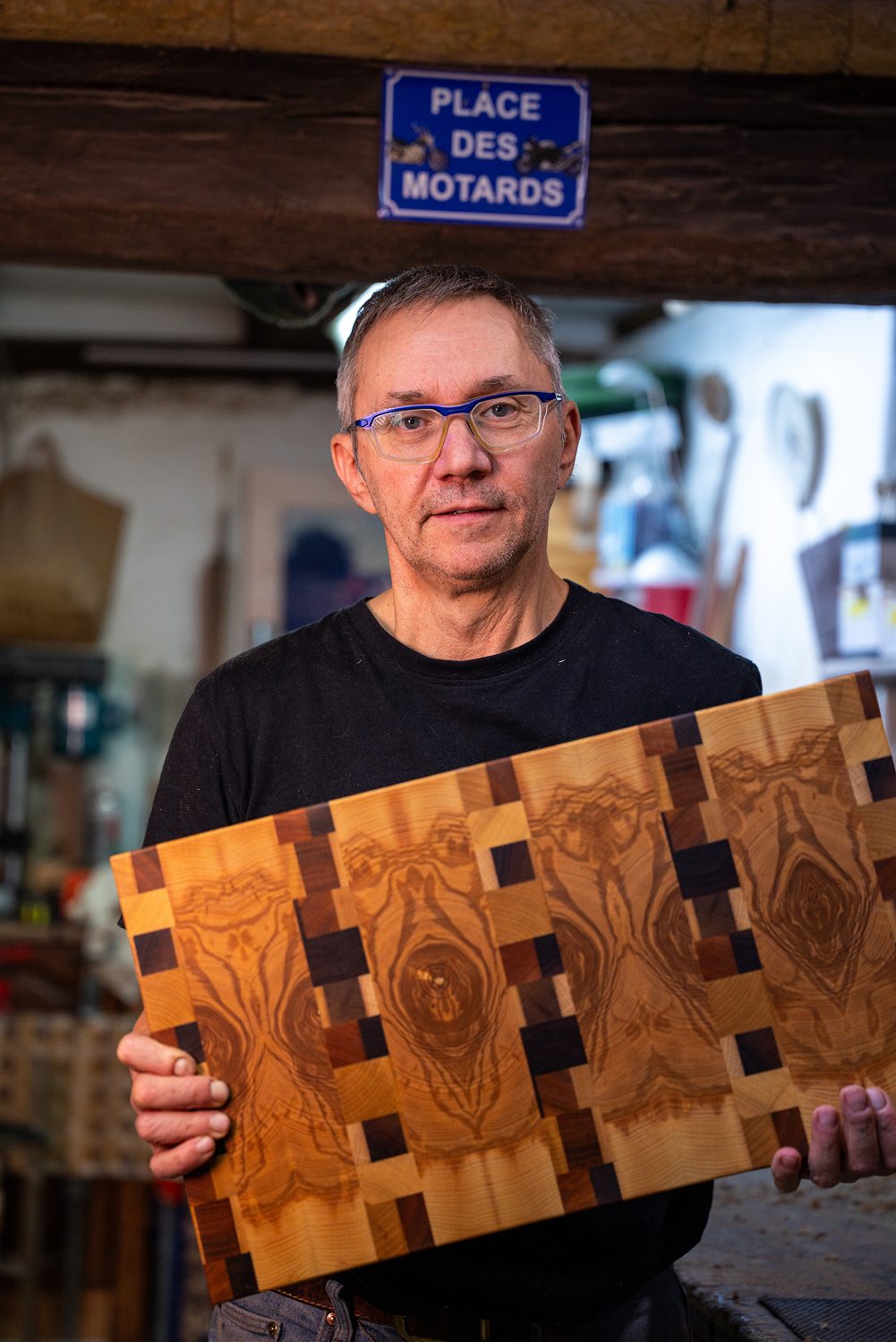 Homme portant des lunettes tenant une planche de bois a motifs complexes.