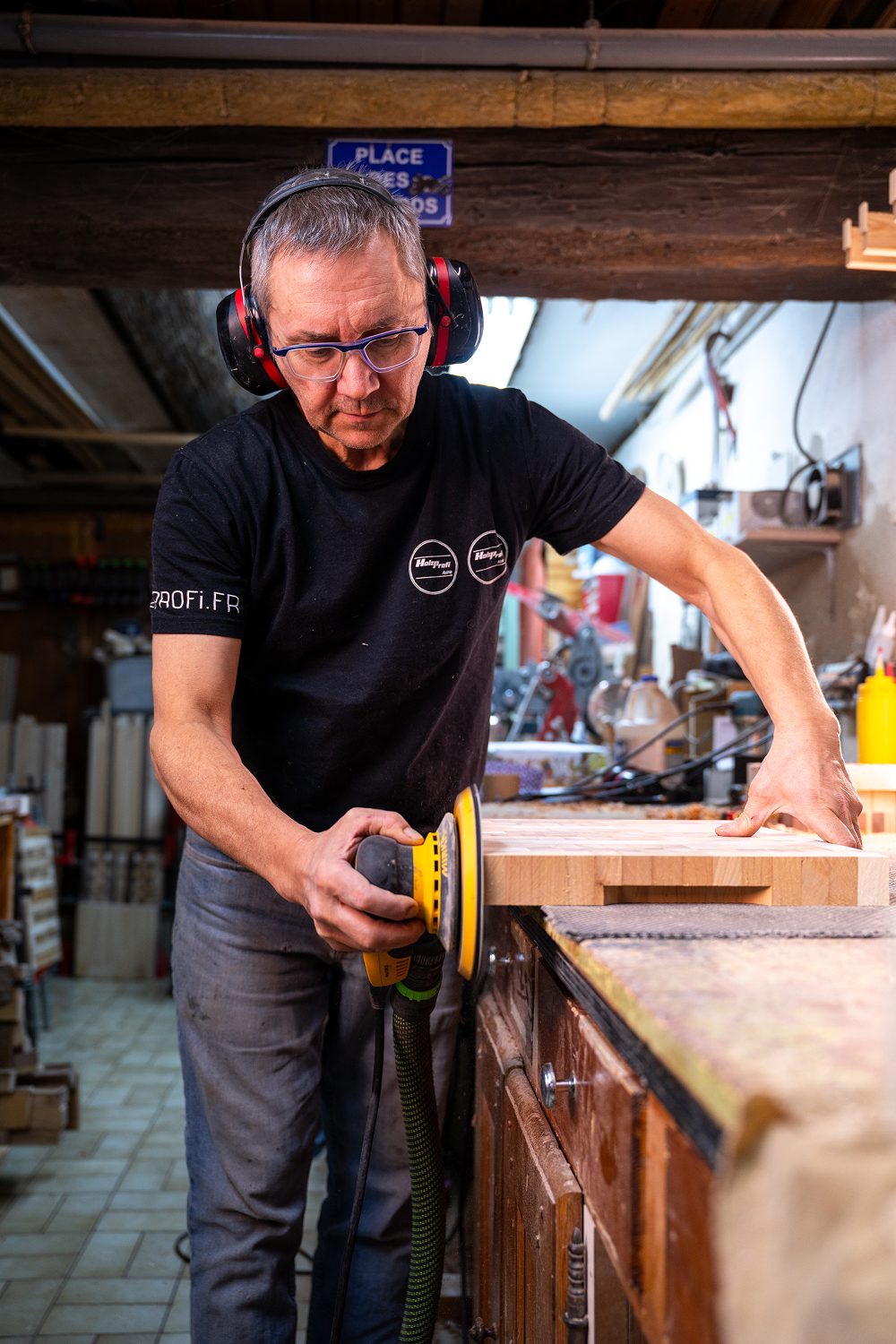 Un homme ponce une planche de bois dans un atelier.