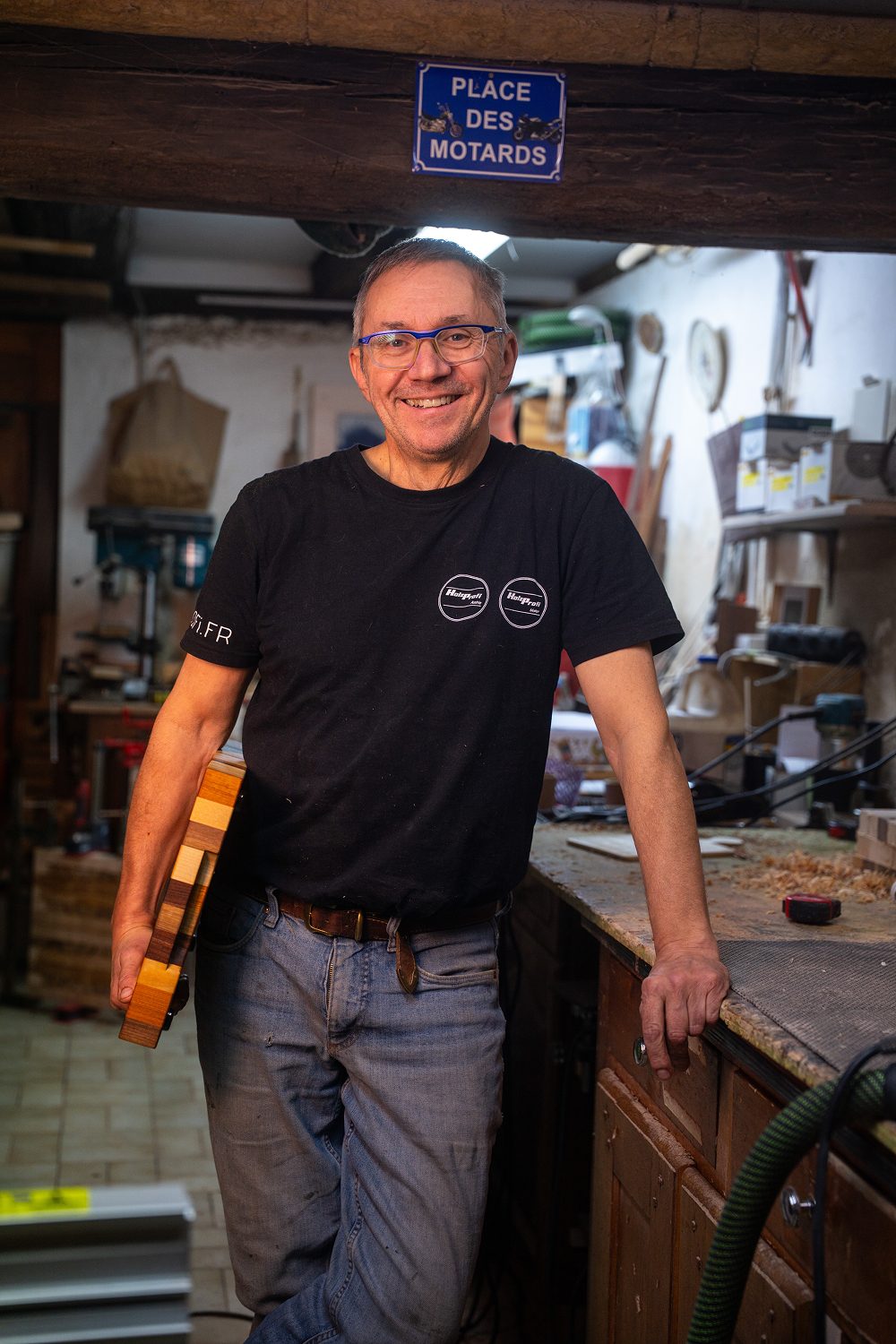 Homme souriant dans un atelier, tenant une planche en bois multicolore.